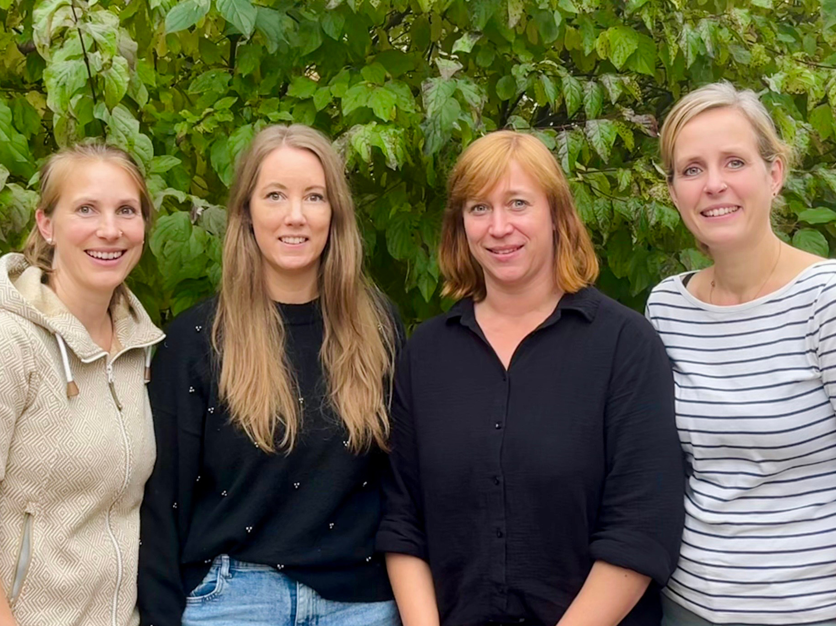 Vier lächelnde Frauen des Elternbeirats vor einer grünen Hecke im Außenbereich der Kita Erdenkinder Wallefeld.